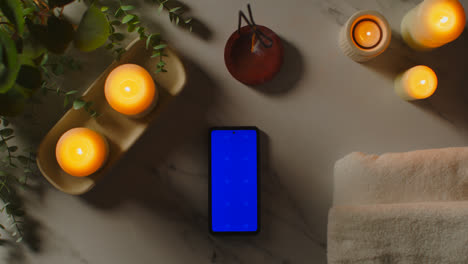 Blick-Von-Oben-Auf-Das-Stillleben-Mit-Bluescreen-Handy-beleuchteten-Kerzen-Und-Räucherstäbchen-Mit-Grüner-Pflanze-Und-Handtüchern-Als-Teil-Der-Spa-Tagesdekoration